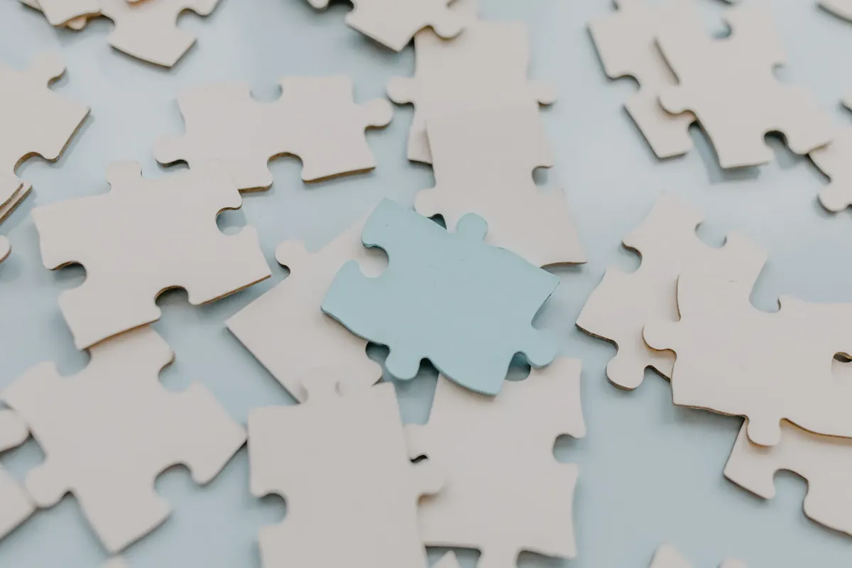 A close-up view of scattered puzzle pieces on a light background, featuring a unique blue piece.