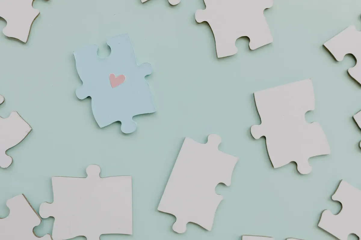 Top view of jigsaw puzzle pieces on a calm green background with a heart on one piece.