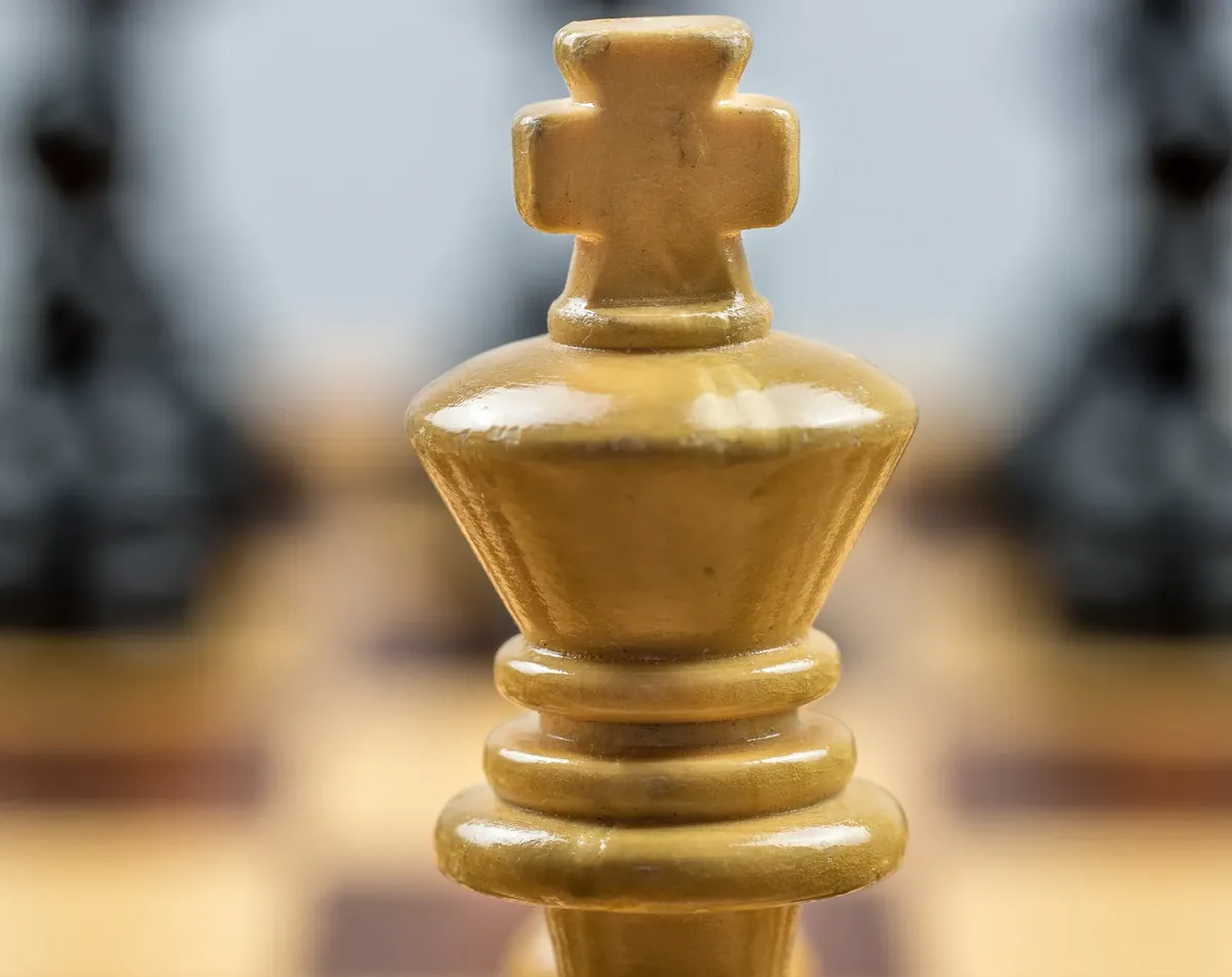 Detailed view of a wooden chess king piece on a chessboard with blurred pieces in the background.