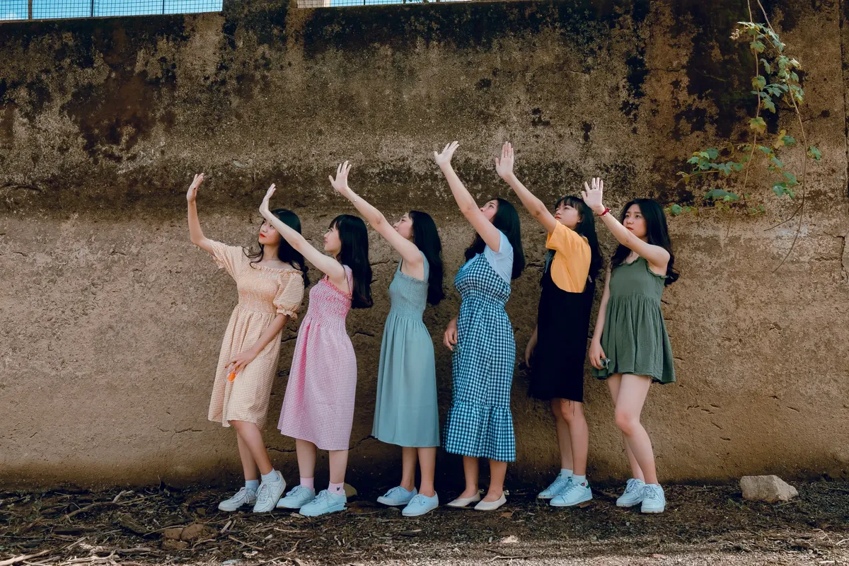 A group of young women dancing playfully outdoors against a rustic wall, expressing joy and friendship.