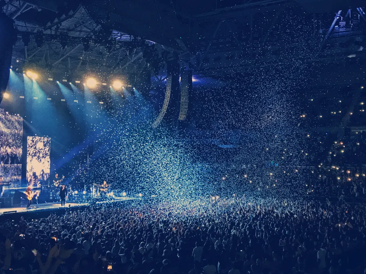 Energetic live concert with confetti and cheering crowd under bright stage lights.