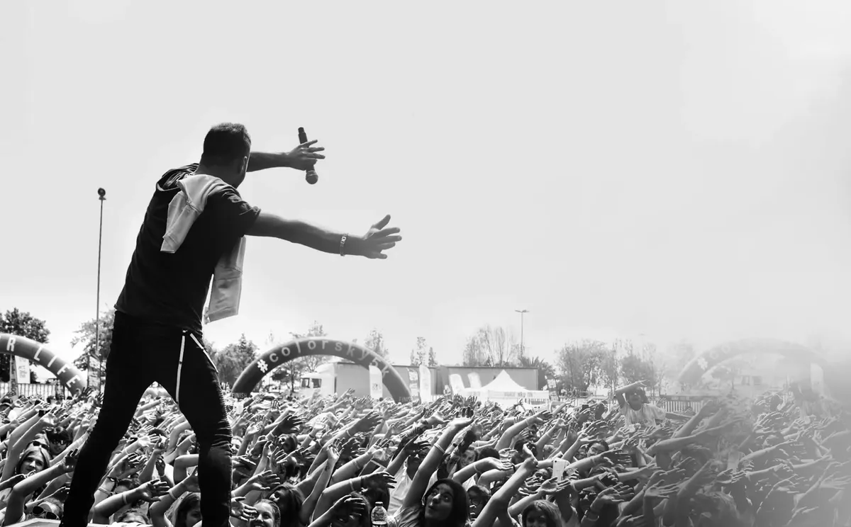 Dynamic black and white image of a live concert with an engaging performer facing a lively crowd outdoors.
