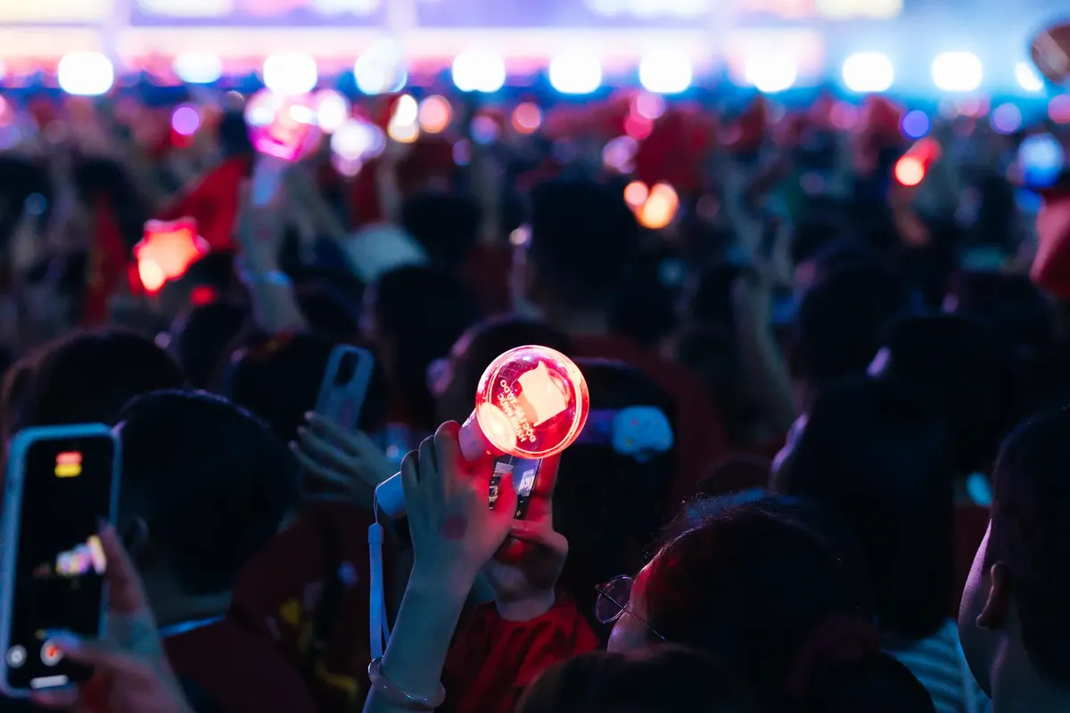 밤에 흐르는 활기찬 콘서트 장면, 관객들이 빨간색 빛을 띤 라이트스틱을 든 상태