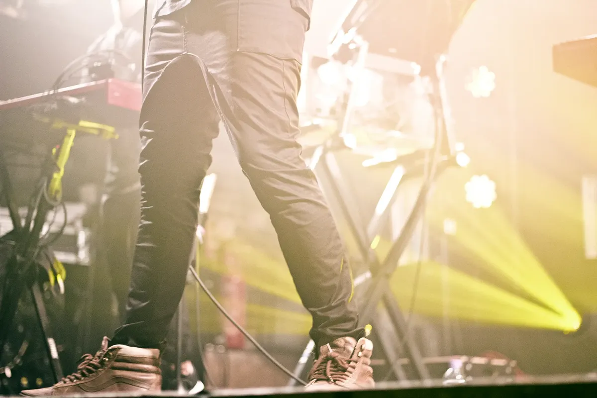 Close-up of a musician's legs during a live performance with vibrant stage lighting.